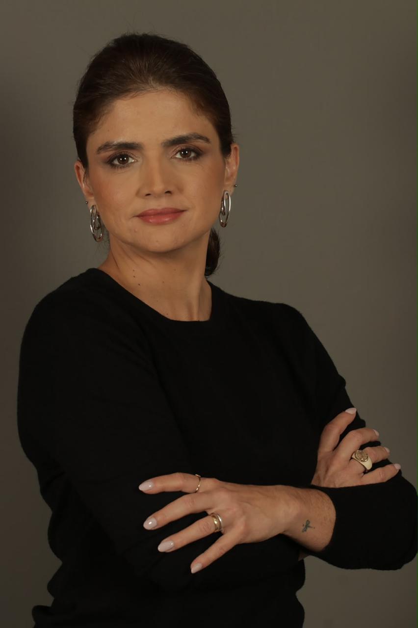 Foto da professora do curso, psicóloga, de braços cruzados, em fundo neutro